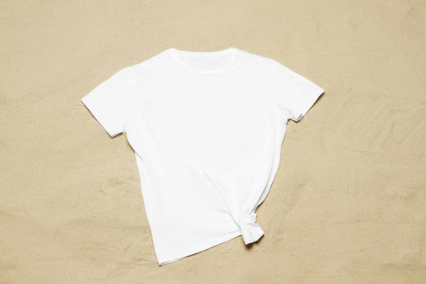 istock Mockup white not wrinkled summer t-shirt copy space. Sand beach texture background. Blank template woman man shirt Top view. Summertime accessories. Flat-lay closeup tshirt on seashore. Beachtime 1605216131