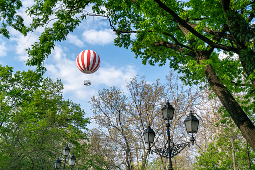 Red white striped hot air balloon seen through a gap among trees of City Park in Budapest on a sunny early summer day