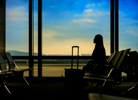 young woman silhouette waiting in airport near her luggage.