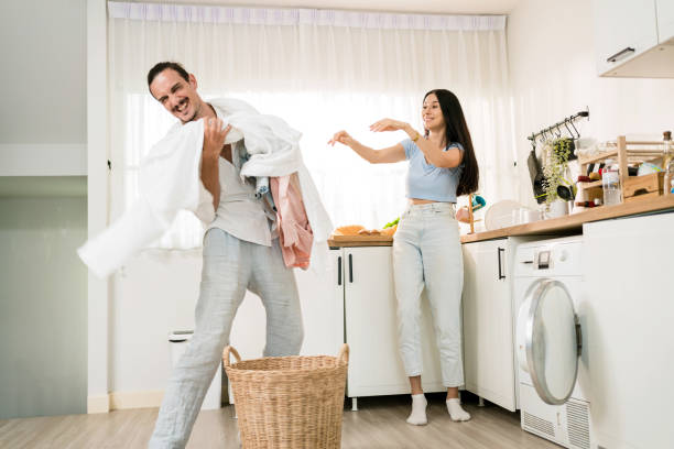 istock Happy Caucasian couple having fun doing laundry together. Couples stand and throw clothes with fun and laugh together before loading them in the washing machine at home. Family doing chores concept. 1605243474