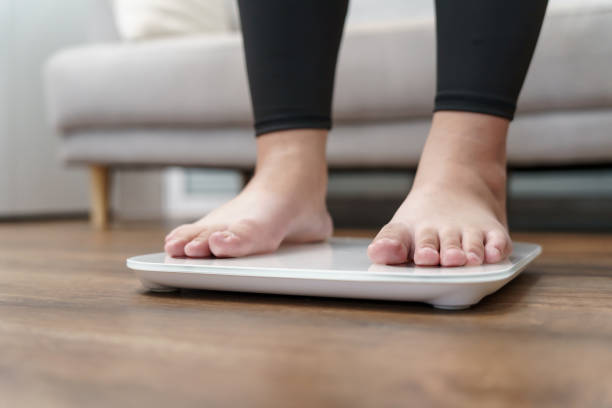 istock Fat diet and scale feet standing on electronic scales for weight control. Measurement instrument in kilogram for a diet control. 1605254710