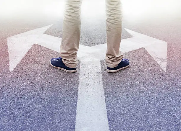 Arrows painted on asphalt. Young man standing hesitating to make a decision.