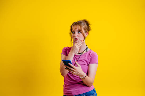 istock Pensive Young Woman Using Phone Against A Yellow Background 1605266445