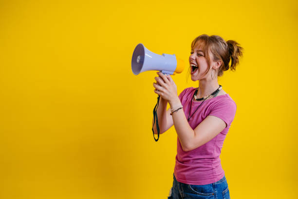 istock Young Woman Talking Into The Megaphone Against A Yellow Background 1605268056