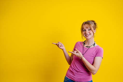 Portrait of a beautiful young woman pointing with her finger while standing in front of a bright yellow background.