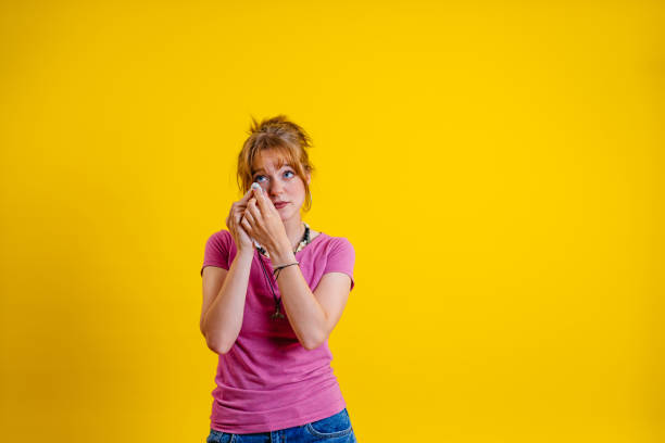 Portrait of a sad young woman crying while standing in front of a yellow background.