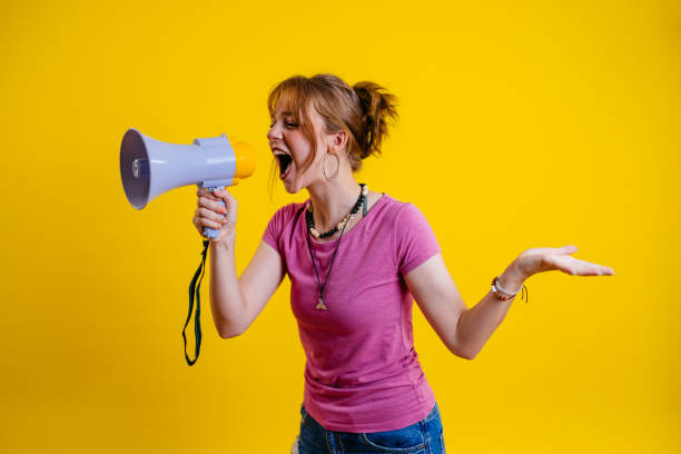 istock Young Woman Talking Into The Megaphone Against A Yellow Background 1605272261