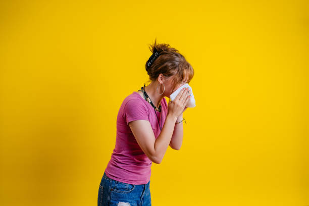istock Young Woman Blowing Her Nose While Standing Against A Yellow Background 1605276072