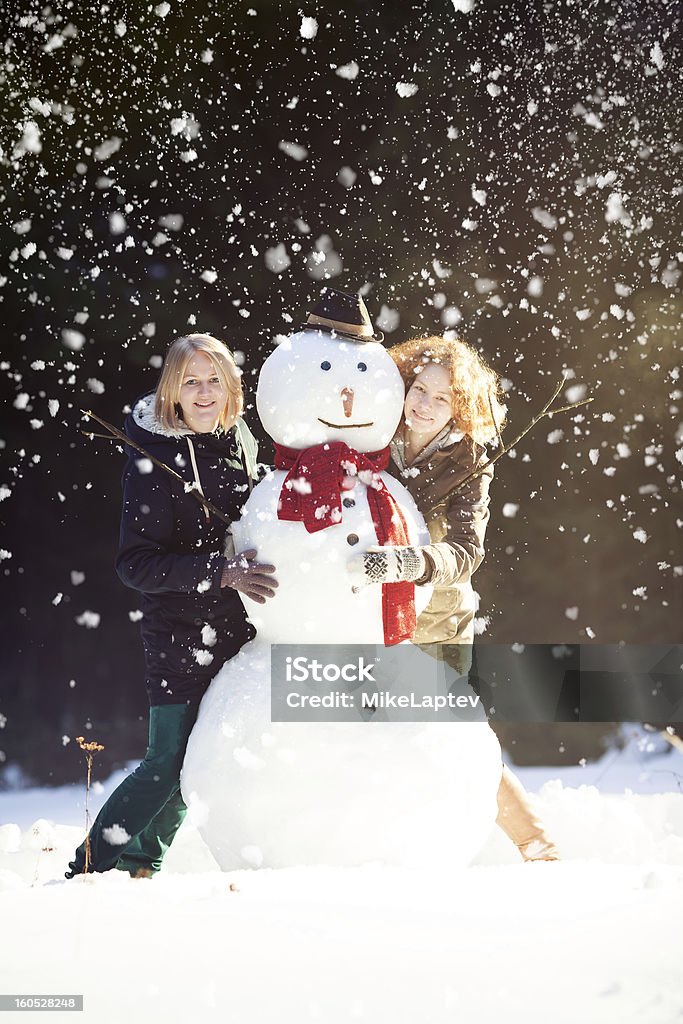 Due giovani donne abbracciare Pupazzo di neve - Foto stock royalty-free di Abbigliamento casual