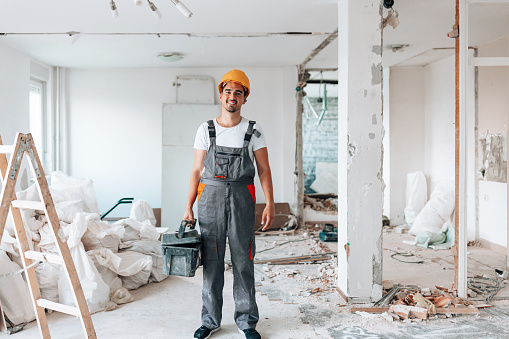 Captured in a compelling portrait, a young construction worker stands confidently within the apartment under renovation, embodying dedication and expertise