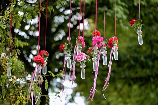 A bouquet of pink flowers in small glass vases hanging in a row on a lamppost in a park. Decorative adornment.