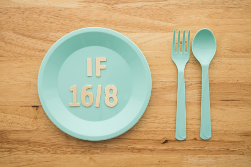 IF (Intermittent Fasting) 16 and 8 diet rule and weight loss concept. IF 16 and 8 letter on blue plate, spoon and fork on wooden table background.
