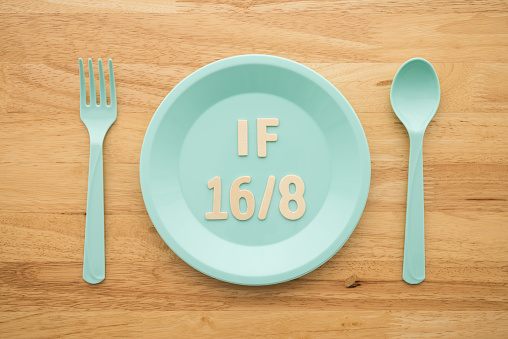 IF (Intermittent Fasting) 16 and 8 diet rule and weight loss concept. IF 16 and 8 letter on blue plate, spoon and fork on wooden table background.