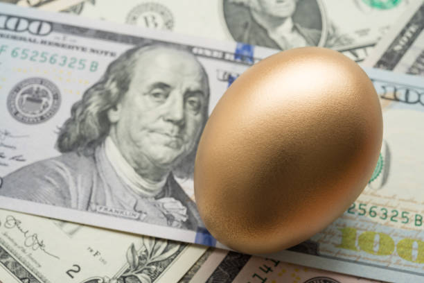 istock Bright golden egg on US dollar bill cash banknotes background. 1605313817