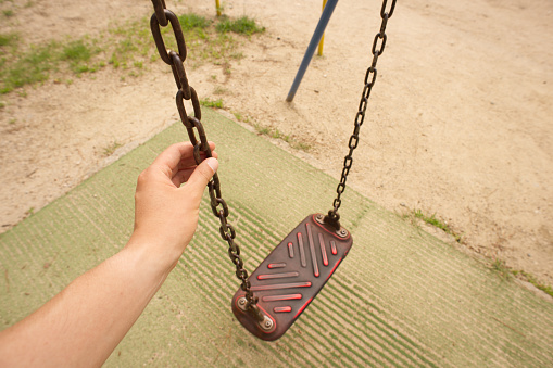 Two children's swing seats hanging by chains in an inner city park. with green grass in the background