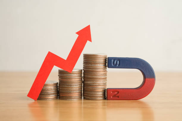 istock Magnet is attracting stacks coins with growth capital gains red graph chart on wooden table. 1605328854
