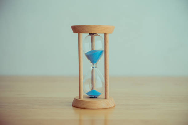istock Hourglass vintage style on wooden table wall background. 1605330522