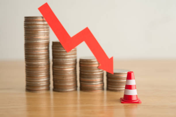 istock Traffic warning cone and stack coins with red chart trending downturn background. 1605330536