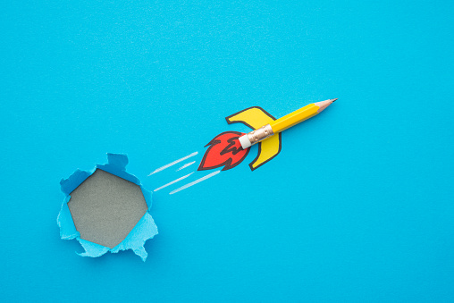 Yellow pencil rocket breaking through hole from obstacle wall to blue zone background minimal style. Concept of breakthrough for new idea, innovative and successful goal in business financial or education.