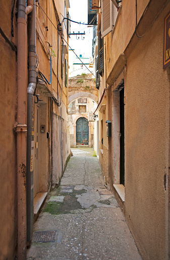 Quiet town backstreet, Corfu Town, Corfu, Greece. Historic Corfu Town (aka Kerkyra) rests halfway down the island’s east coast. A town of Venetian architectural grace and elegance, the name means ‘peaks’, referring to its twin hills, each with by a massive fortress to repel Ottoman sieges. The Old Town is a warren of winding lanes, with restaurants,bars and shops as well as timeless back alleys. The Island of Corfu, Greece. Corfu, or Korkyra, lies to the west of the Greek and Albanian mainland and separates the Adriatic from the Ionian Seas. Largely formed from Limestone, the island measuring some thirty miles by 18 miles is now a tourist destination, known for its beaches, climate and olives. Medieval castles and ancient ruins chart the military history of the island back to ancient Greek mythology.