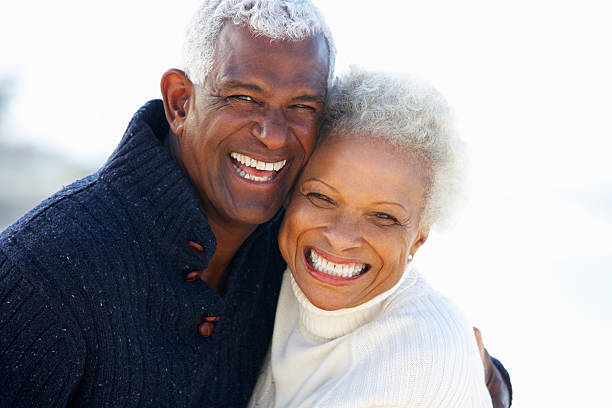 sorridente casal sênior abraçando na praia - retirement couple beach senior adult - fotografias e filmes do acervo