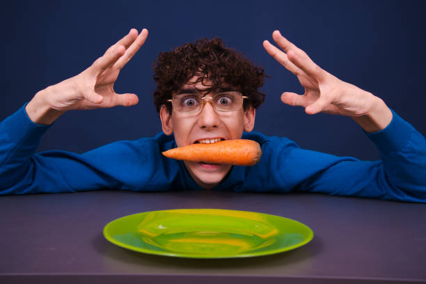 istock Funny silly guy eats carrots. Diet and healthy lifestyle. 1605385488