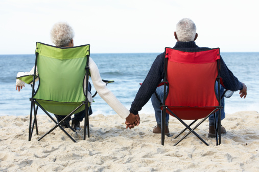Senior Couple Sitting On Beach In Deck chairs Holding Hands