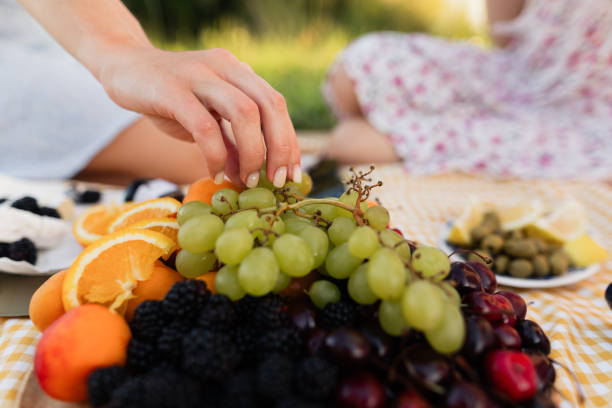 istock Unrecognizable female hands take grapes from a plate at a picnic on a sunny day 1605392108