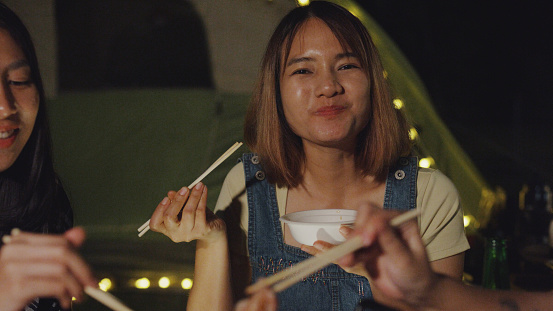 Closeup group of happy Asian friends having barbecue grill together in vacation with camping caravan at night. Lifestyle travel nature concept.