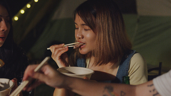 Closeup group of happy Asian friends having barbecue grill together in vacation with camping caravan at night. Lifestyle travel nature concept.