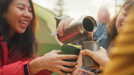 Closeup group of happy Asian friends drinking a cup of hot coffee for breakfast in vacation with camping caravan at morning. Lifestyle travel nature.