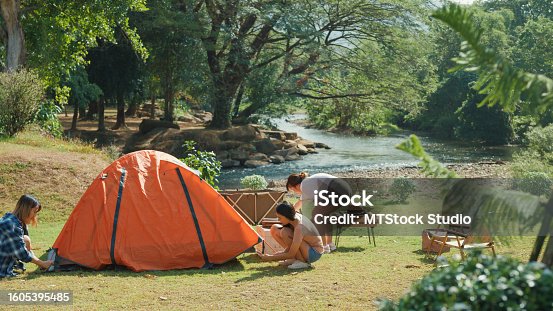 istock Group of happy Asian friends setting up the camp tent near stream in vacation with camping caravan at morning. Lifestyle travel nature. 1605395485