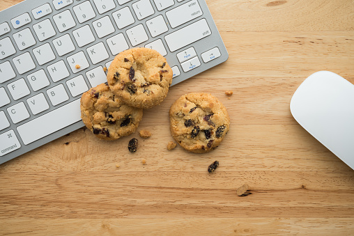 Flat lay of white chocolate chip cookies on keyboard computer and mouse on wooden table background copy space. Cookies website internet homepage policy accpeted or blocks concept.