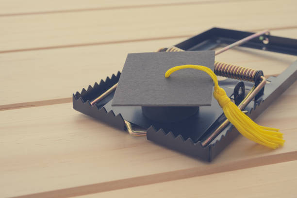 istock Graduation cap in a mousetrap on wooden table background. 1605396850
