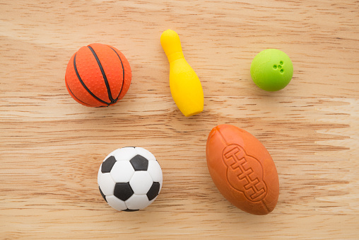 Flat lay of cute sport balls (basketball, bowling, soccer, rugby) eraser toy set on wooden background minimal style. Kids learning by play sport for development and exercise concept.