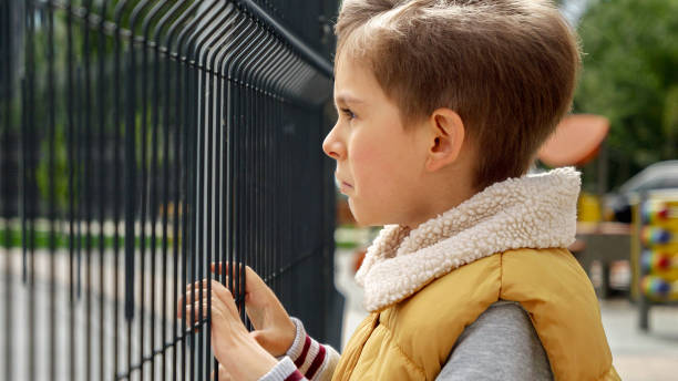 istock Upset and lonely boy standing on public playground and looking through it. Child depression, problems with bullying, victim in school, emigration, criminal and poverty 1605402462