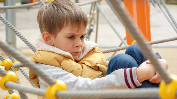 Upset and sad little boy being victim of bullying sitting alone on school playground. Child depression, problems with bullying, victim in school, emigration, criminal and poverty Upset and sad little boy being victim of bullying sitting alone on school playground. Child depression, problems with bullying, victim in school, emigration, criminal and poverty. sad teenager boy crying outdoors in park stock pictures, royalty-free photos & images