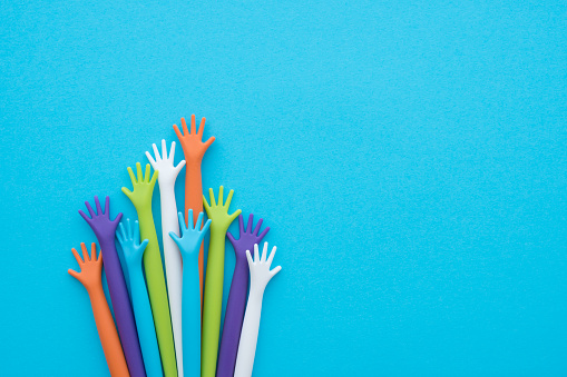 Many colorful hands up on blue background with copy space. Concept of international human rights, equality and peace. Color hands are symbol of diversity.