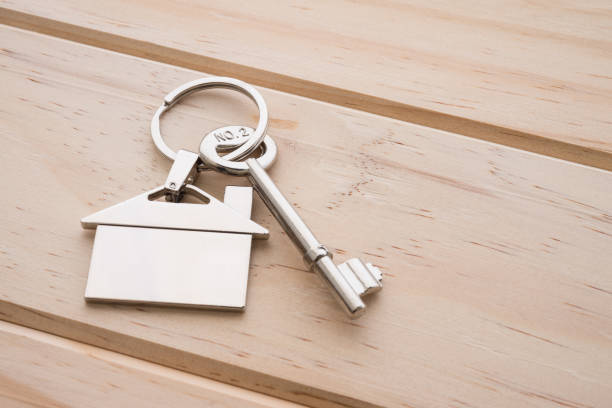 istock Silver house key with house keychain on wooden background with copy space. 1605410277