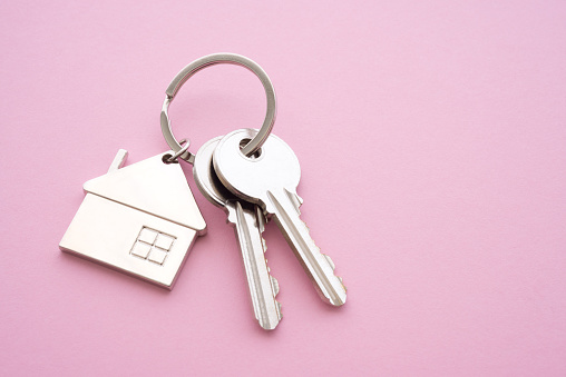 Silver house key with house keychain on pink background with copy space. Dream new house buying, real estate property business, banking concept.