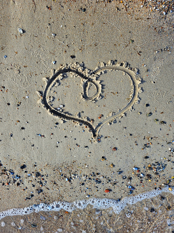 Romantic honeymoon holiday or Valentine's day on the beach concept with two hearts drawn on the sand, tropical getaway for couples, love symbol