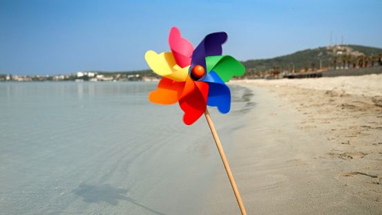 Colorful pinwheel spinning in the wind on a sandy beach, evoking the concepts of travel, summer holiday, vacation, beach tourism, and joy