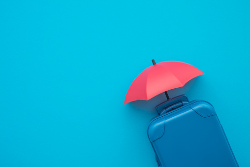 Red umbrella cover suitcases travelers on blue background copy space. Travel insurance business concept. Travel insurance covers loss suitcase, flight delays, cancellations, accident, medical expenses.