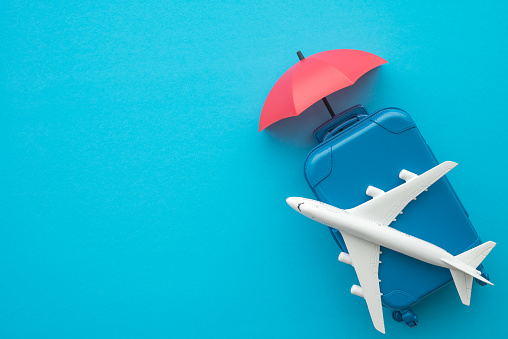 Travel insurance business concept. Red umbrella cover airplane and suitcases travelers on blue background. Travel insurance covers loss suitcase, flight delays, cancellations, accident and medical expenses.