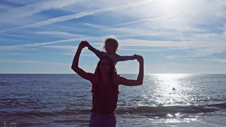 Mother carry little girl on shoulders, turn, spin at sea beach