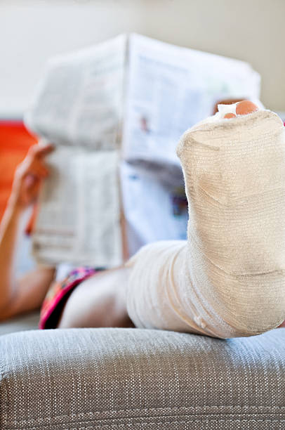 istock Woman with broken leg lying on sofa and reading newspaper 160544333