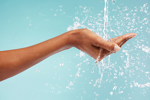 Hands, woman and water splash for washing, skincare and healthy beauty on studio background. Closeup of person cleaning body, drops and palm in bathroom for wellness, shower and aesthetic self care