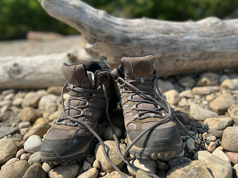 Untied brown hiking shoes with socks inside of them, tucked in, resting on pebbles at the lakeshore. No people. Taken in Northern Wisconsin.