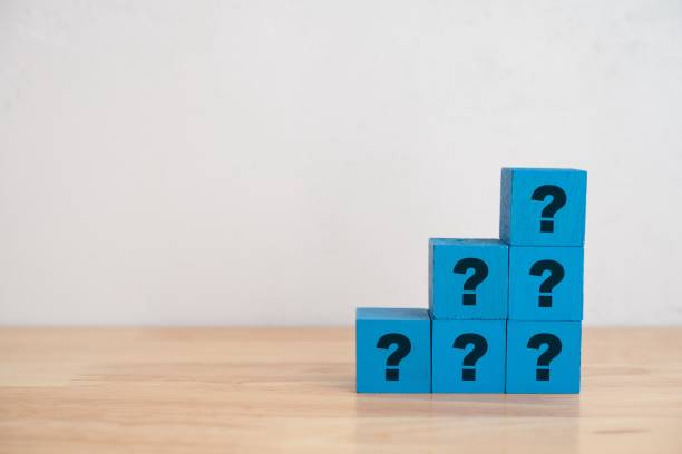 istock Blue wooden cube block stacking as staircase with sign question mark ? on wooden table. 1605471512
