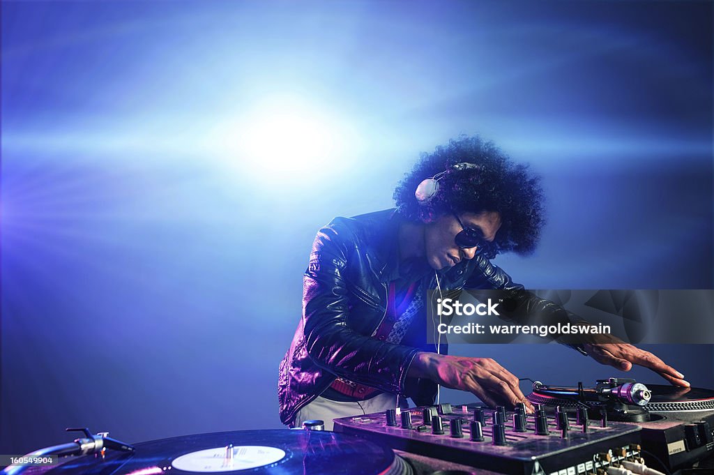 DJ playing in a nightclub with lights behind them nightclub dj playing music on deck with vinyl record headphones light flare clubbing party scene DJ Stock Photo